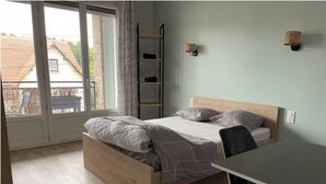 A bedroom with a wooden bed, a desk, and a window with a view of a house. - Chill & relax (Limoges)