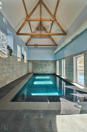 Una piscina interior con vistas despejadas al cielo a través de amplias ventanas, una pared de piedra y una estructura de techo de madera.