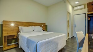 Une chambre d’hôtel comprenant un lit, une table de chevet, une chaise et un bureau avec une autre chaise.