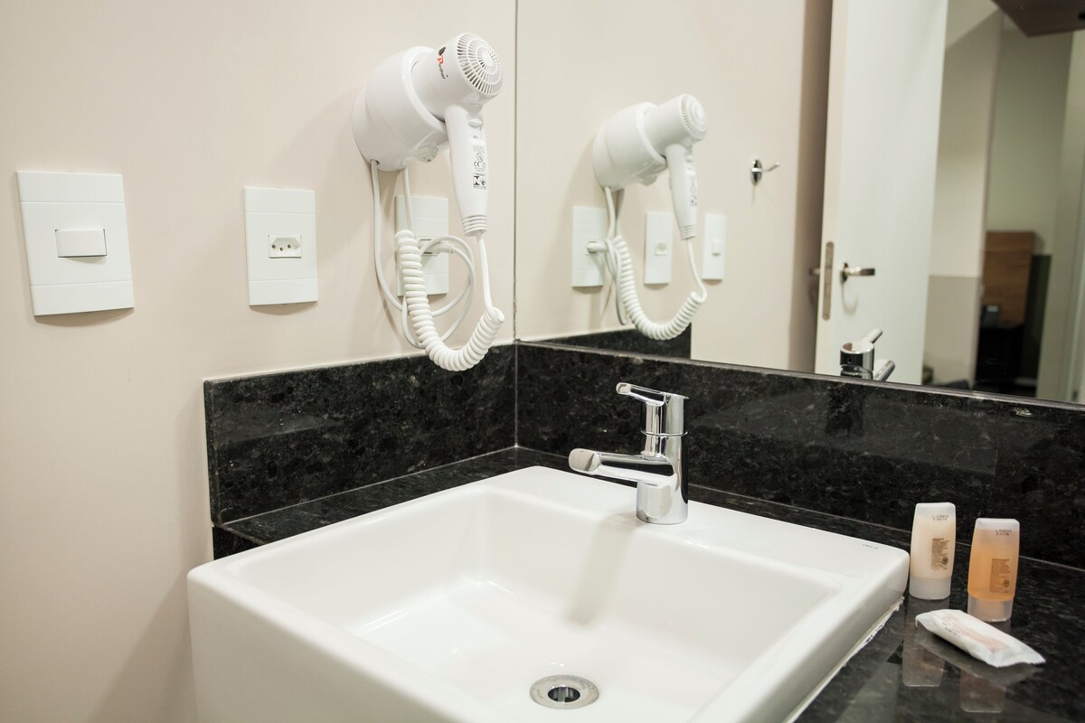 A bathroom with a white sink, a mirror, and two hair dryers mounted on the wall.