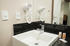 A bathroom with a white sink, a mirror, and two hair dryers mounted on the wall. - Transamerica Wise Indaiatuba (Indaiatuba)