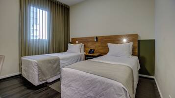 Habitación de hotel con dos camas, cabecera de madera, mesita de noche con teléfono y ventana con cortinas.