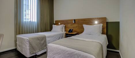 A hotel room with two beds, a wooden headboard, a bedside table with a phone, and a window with curtains.