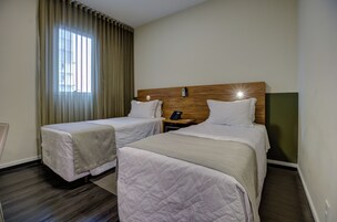 Habitación de hotel con dos camas, cabecera de madera, mesita de noche con teléfono y ventana con cortinas.