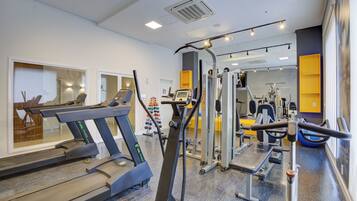 Un gimnasio con cintas de correr, máquinas de pesas y un muro con espejos.