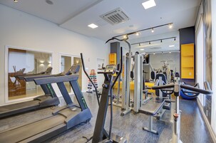 Un gimnasio con cintas de correr, máquinas de pesas y un muro con espejos.