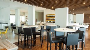 A modern hotel lobby with round tables and black chairs, a bar area with shelves of bottles, and a seating area with a tufted sofa.
