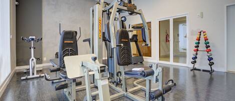 A gym with various exercise equipment, including a squat rack, a bench press, and a cable machine.