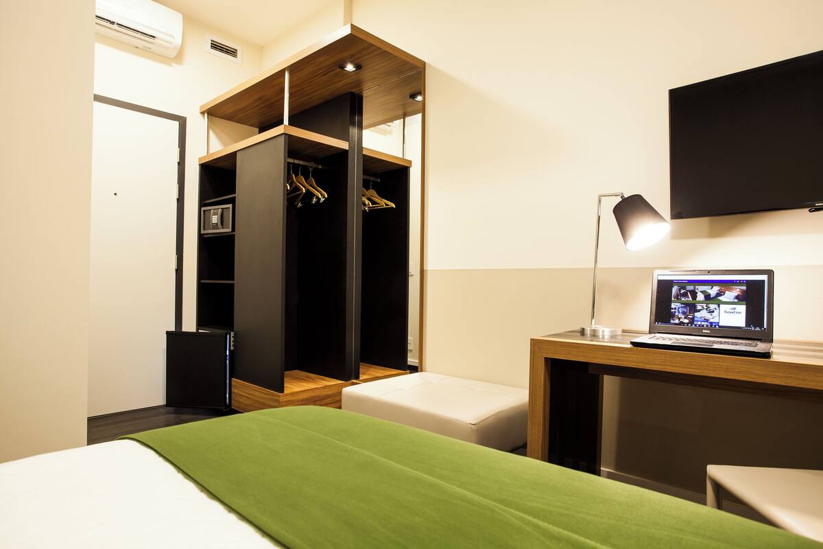 Une chambre d’hôtel comprenant un lit, un bureau avec un ordinateur portable, une télévision, une armoire et une table de chevet.