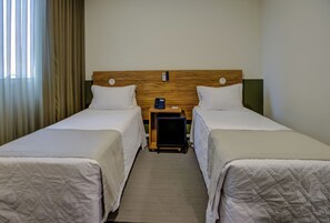 A hotel room with two beds, a wooden headboard, a bedside table with a phone, and a window with curtains. - Transamerica Wise Indaiatuba (Indaiatuba)