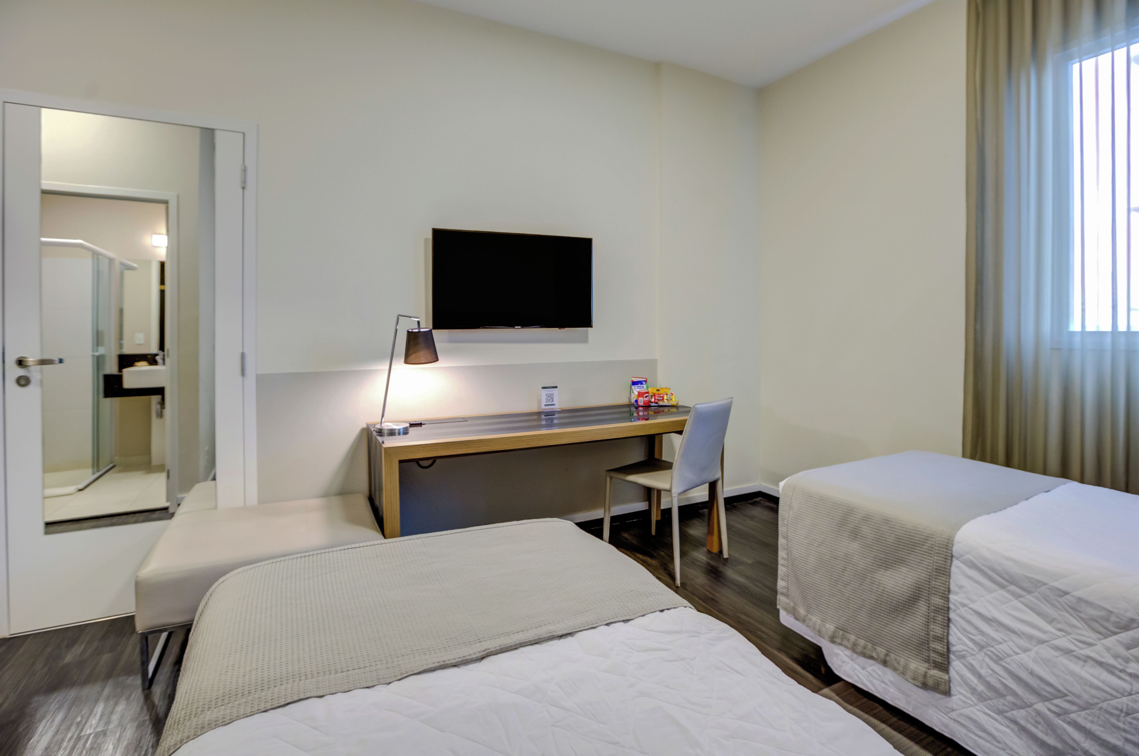 A hotel room with a bed, a desk, a chair, a television, and a window with curtains.