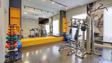 Une salle de sport équipée de divers appareils d’exercice, d’un miroir et d’un téléviseur fixé au mur.