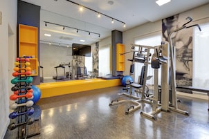 Un gimnasio con varios equipos de ejercicio, un espejo y un televisor en la pared.