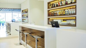 A modern bar area with a white counter, wooden accents, and multiple shelves of liquor bottles.