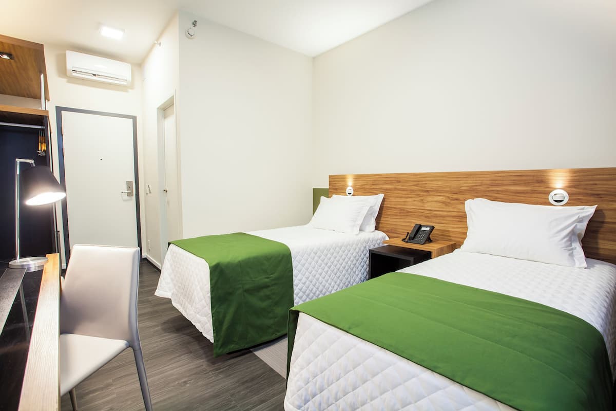 Une chambre d’hôtel avec deux lits, un bureau, une chaise et une table de chevet avec un téléphone.