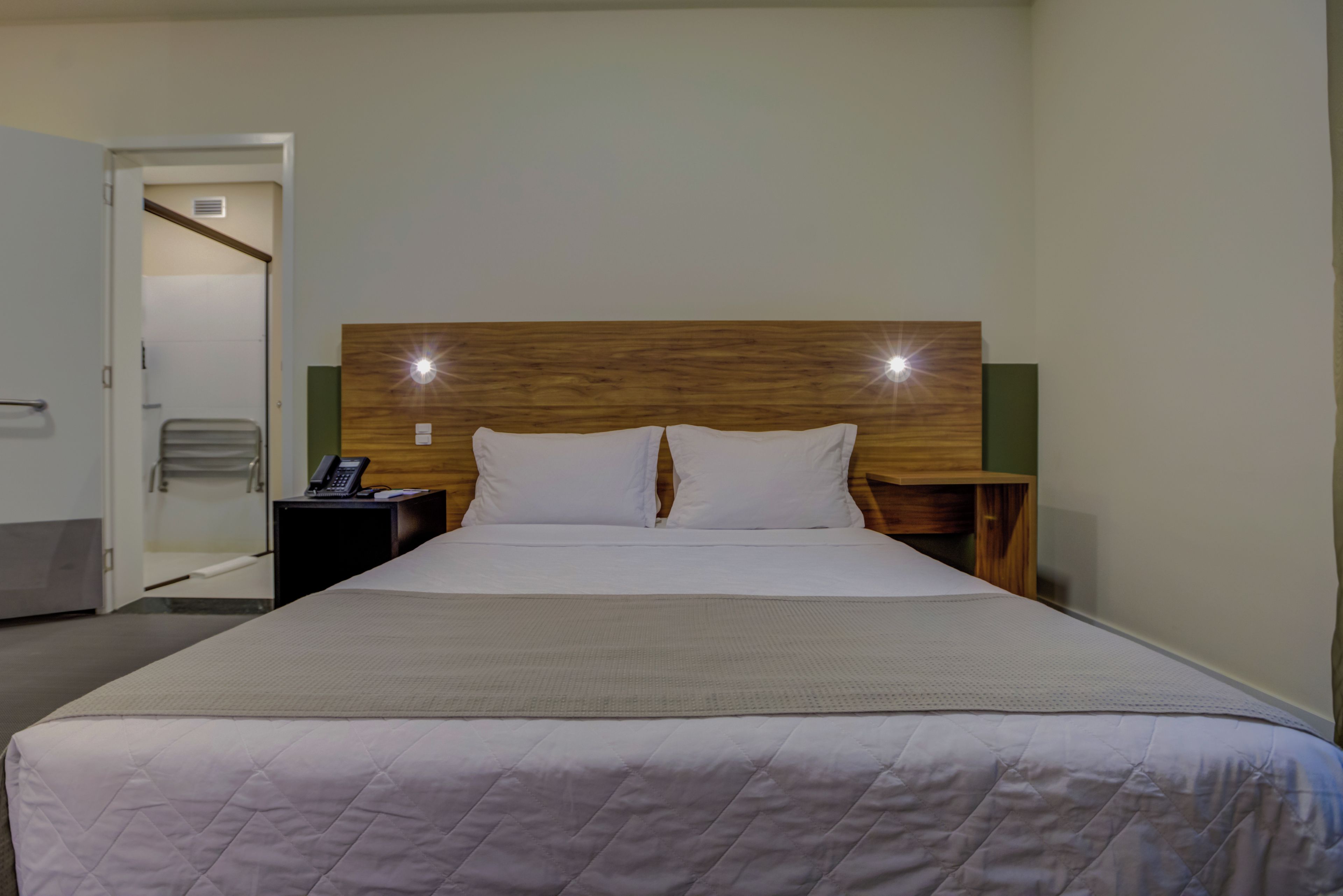 Quarto de hotel com uma cama grande, cabeceira de madeira, duas mesas de cabeceira e um telefone em uma delas.