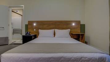Quarto de hotel com uma cama grande, cabeceira de madeira, duas mesas de cabeceira e um telefone em uma delas.