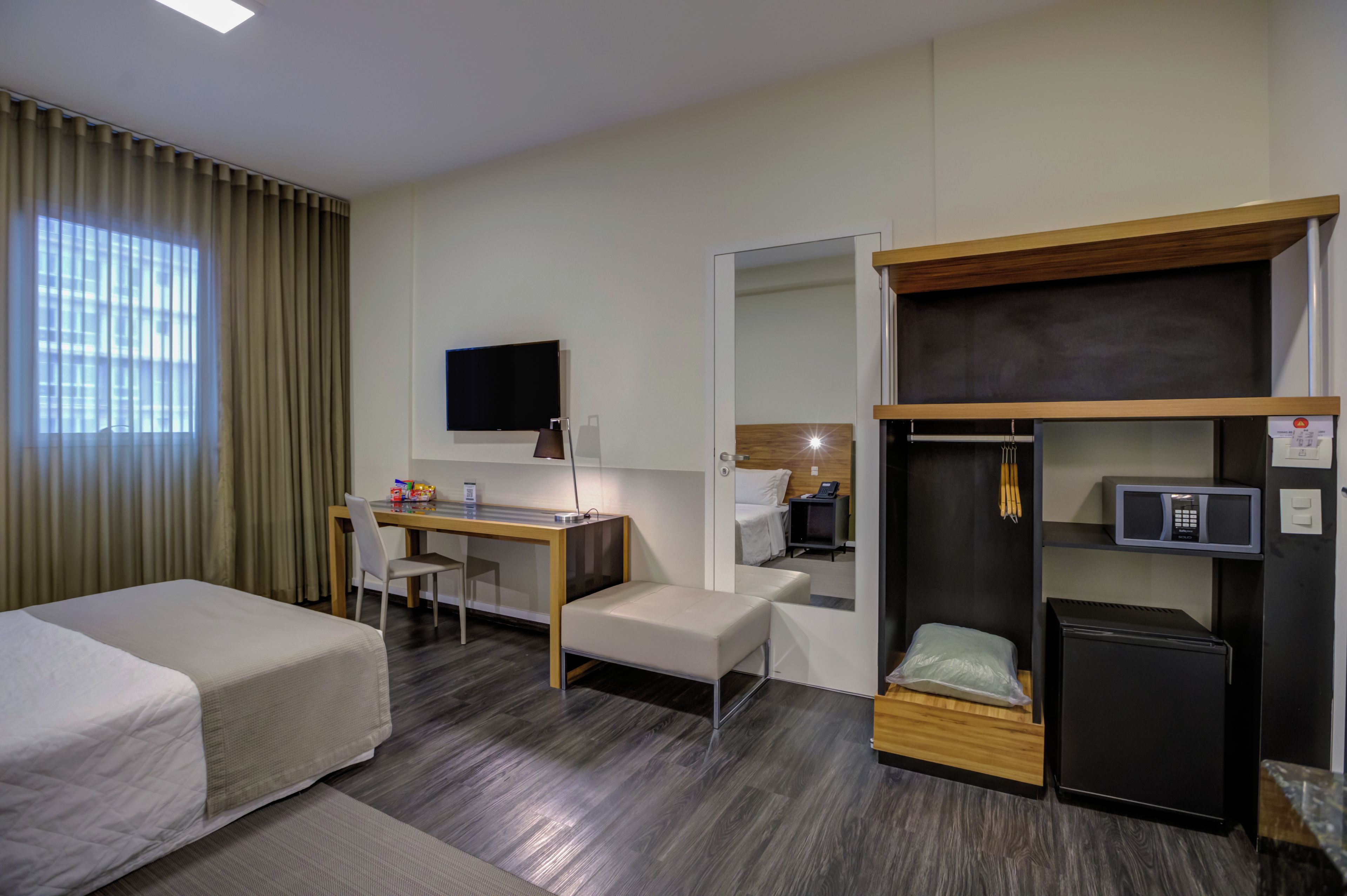 A hotel room with a bed, a desk, a chair, a television, a wardrobe, and a microwave.