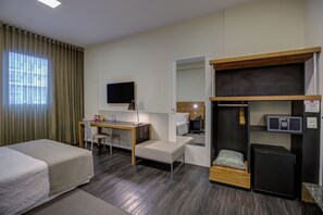 Une chambre d’hôtel équipée d’un lit, d’un bureau, d’une chaise, d’une télévision, d’une armoire et d’un four à micro-ondes.