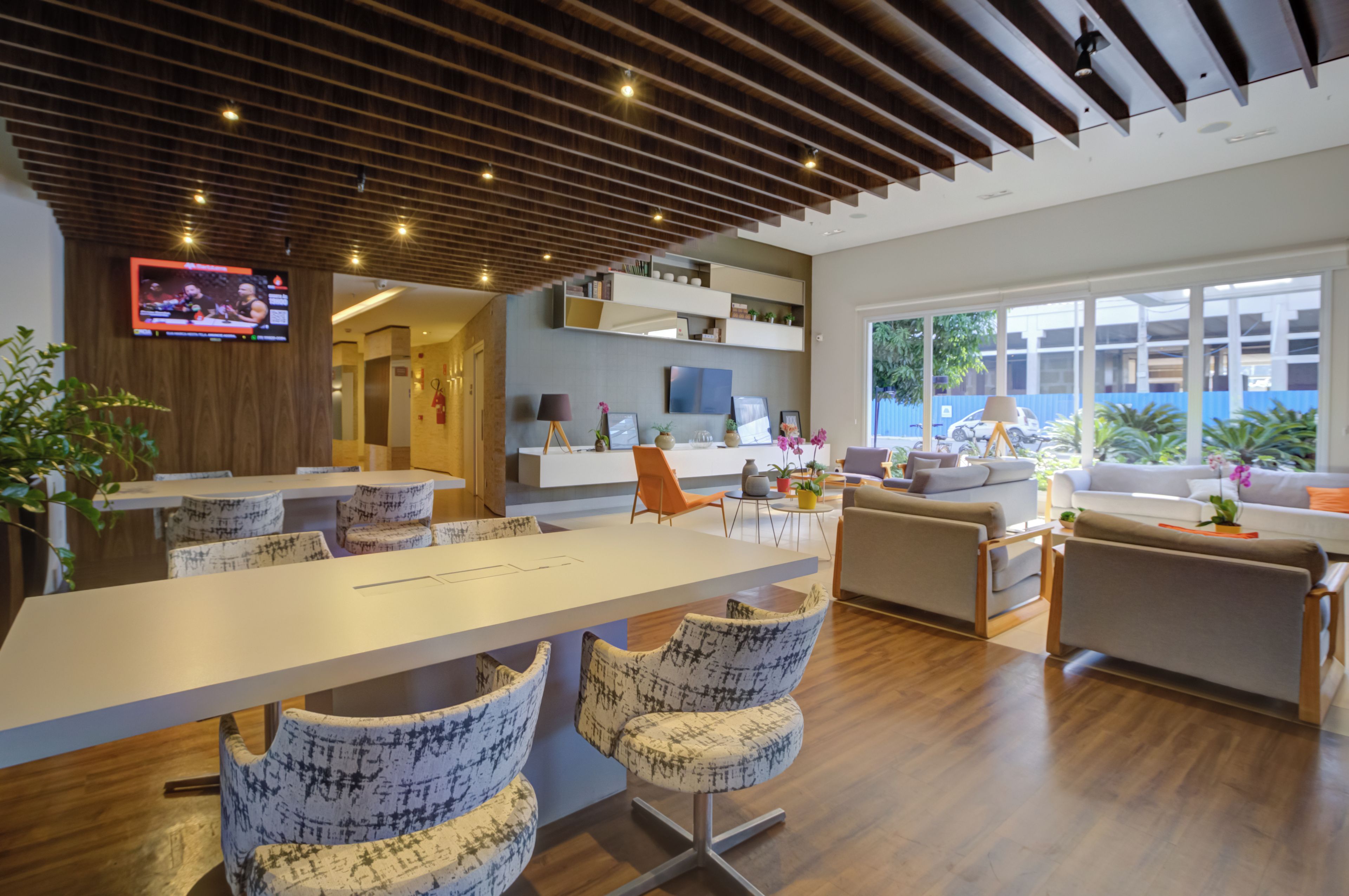 Sala de estar moderna com área de jantar, TV fixada na parede e uma grande janela com vista para o exterior.
