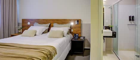Habitación de hotel con cama, mesita de noche y baño con cabina de ducha de vidrio.