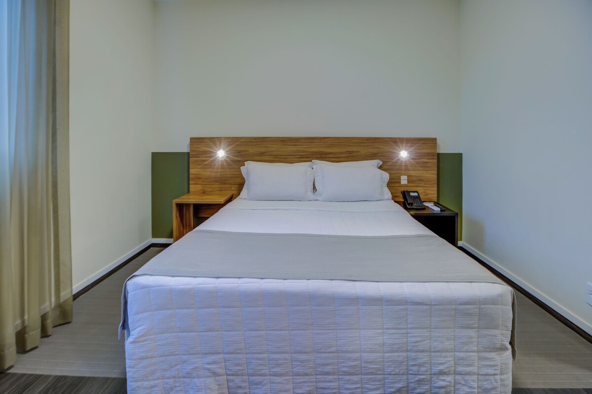 A hotel room with a bed, a nightstand, a telephone, and a wall-mounted light fixture.