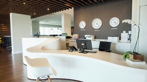 A modern reception desk with a curved design, multiple clocks displaying different time zones, and a potted orchid on the right.
