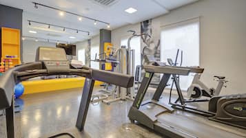 Academia com esteiras, equipamentos de exercício e uma grande janela.