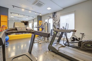 Academia com esteiras, equipamentos de exercício e uma grande janela.