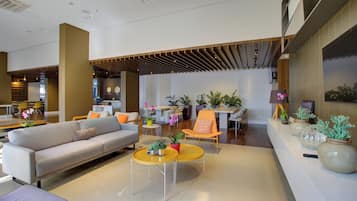 A modern interior with a sofa, coffee table, and chairs. There are plants and a clock on the wall.