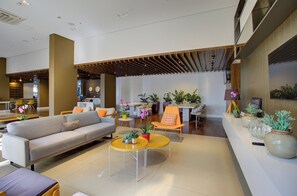 A modern interior with a sofa, coffee table, and chairs. There are plants and a clock on the wall. - Transamerica Wise Indaiatuba (Indaiatuba)