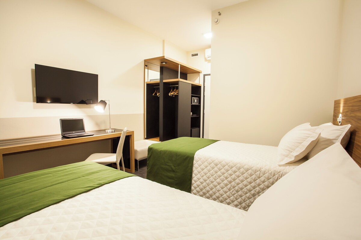 A hotel room with two beds, a desk with a laptop, a TV, and a wardrobe.