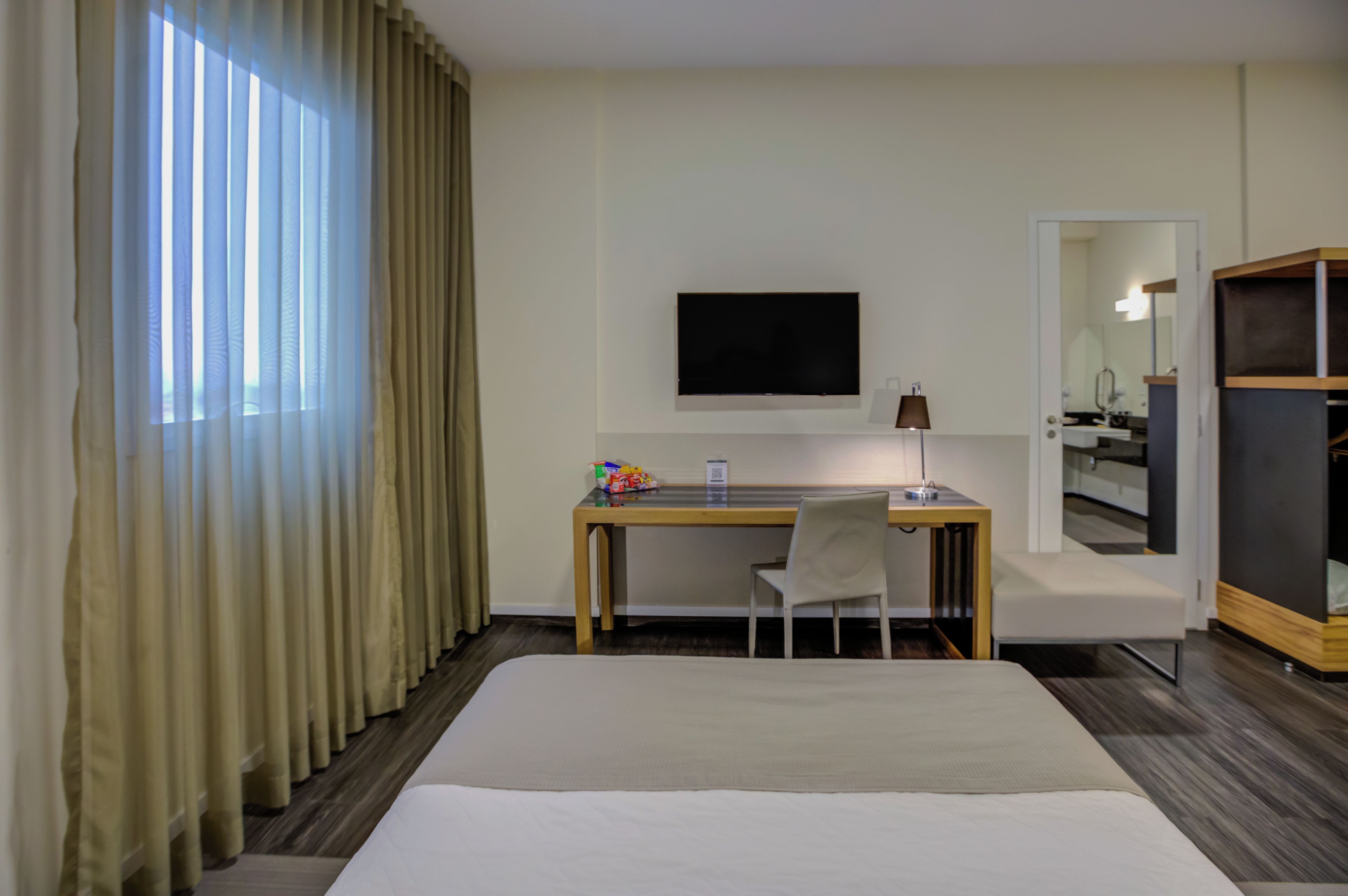 Ett hotellrum med en säng, ett skrivbord med en stol, en tv och en spegel.