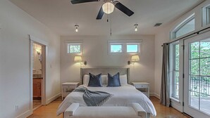A spacious bedroom with a large bed, two bedside tables, a ceiling fan, and a view through the large window. - 5BR Retreat in Bouldin Creek | Walk to SoCo (Austin)