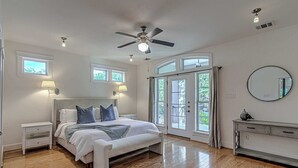 Una camera da letto con un letto, comodini, una ventola a soffitto e vista attraverso una porta vetrata.