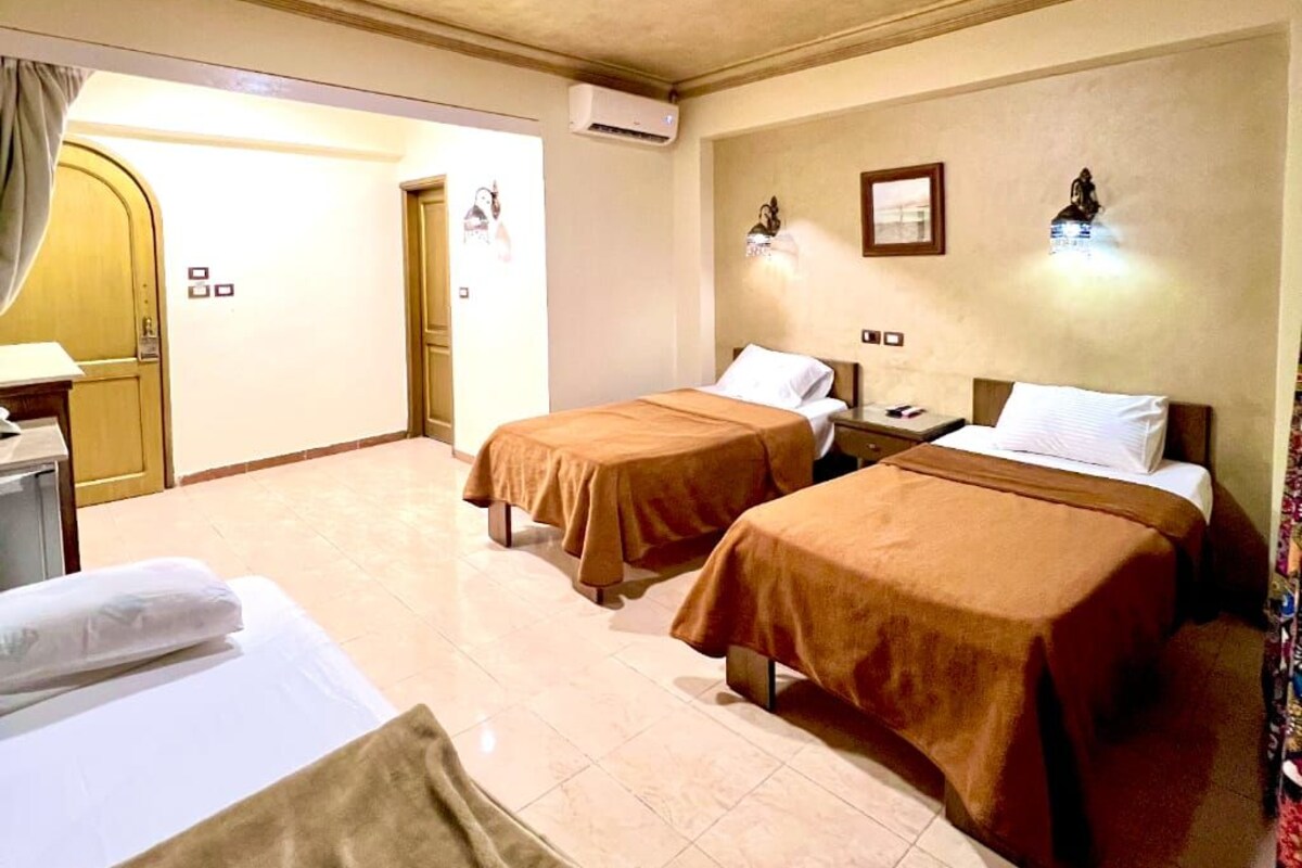 A hotel room with two beds, a desk, a chair, and a door leading to another room.