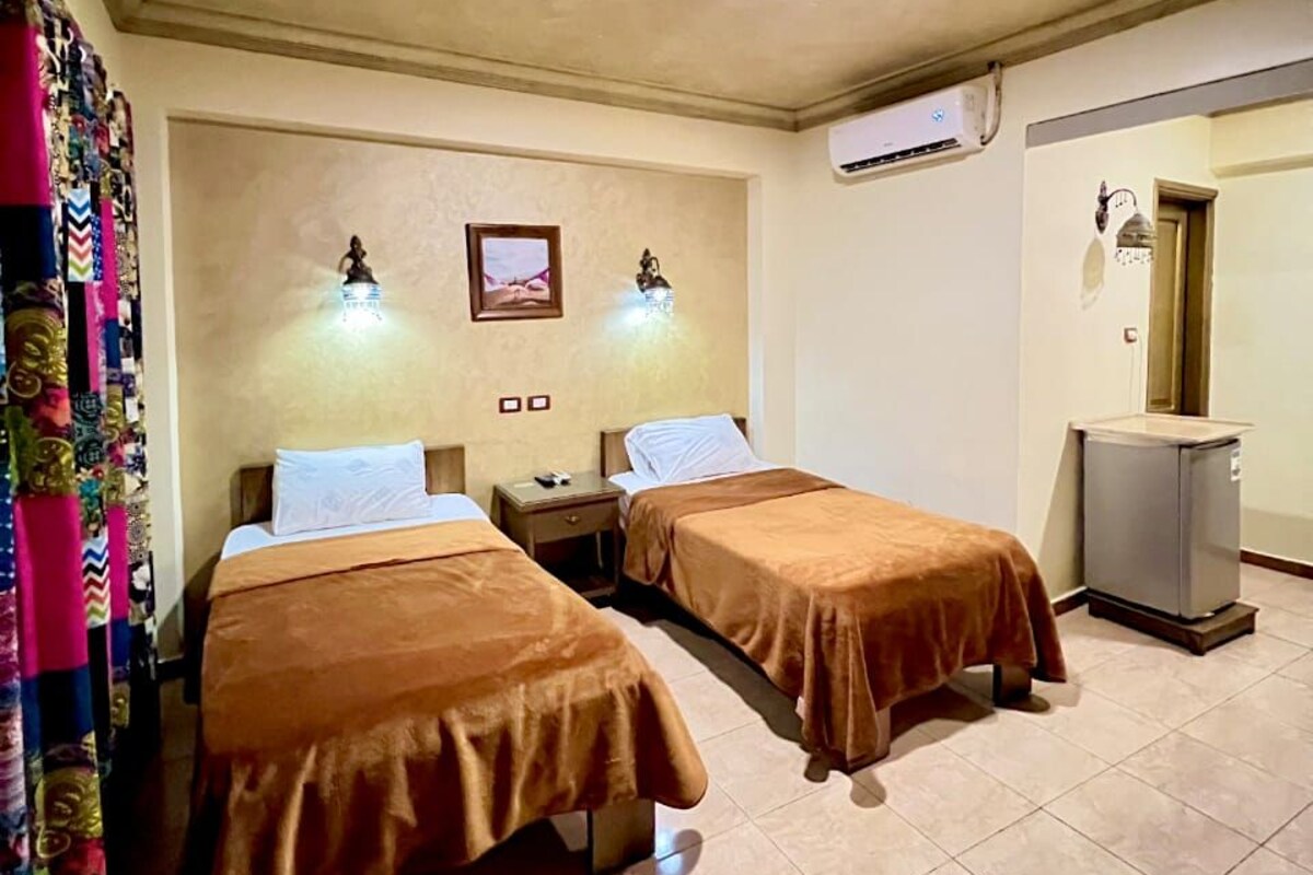 A hotel room with two beds, a ceiling light, an air conditioning unit, and a small table.