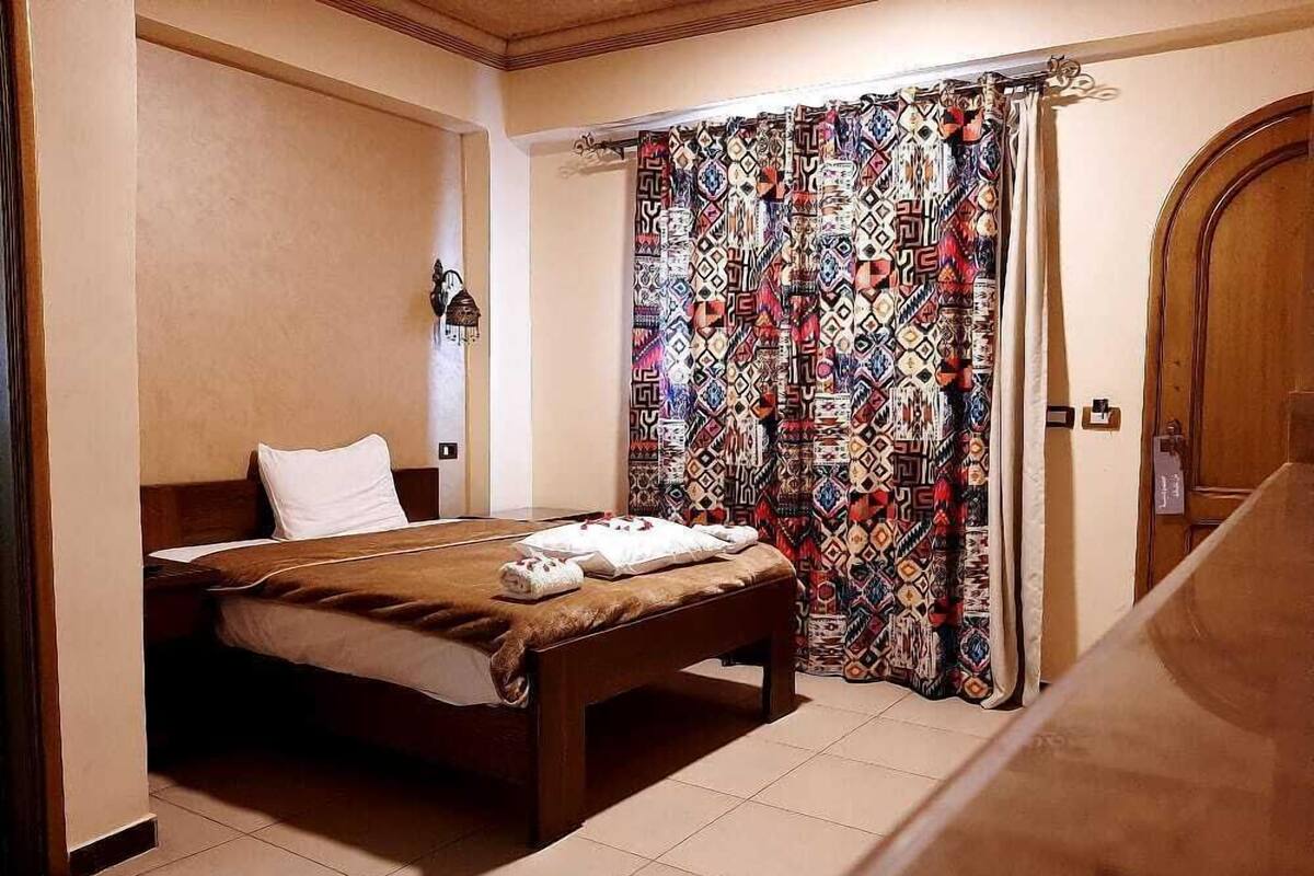 A bedroom with a bed, a bench, a patterned curtain, and a wooden door.