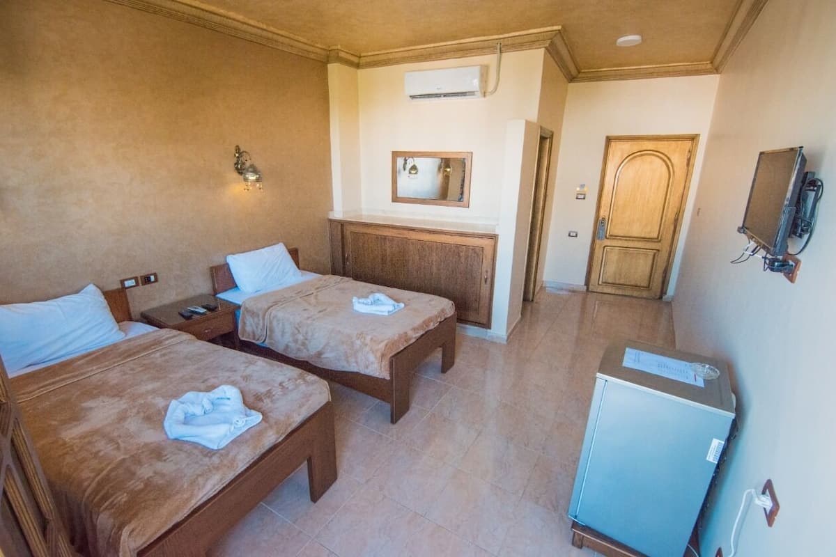 A hotel room with two beds, a small desk, a mirror, and a television.