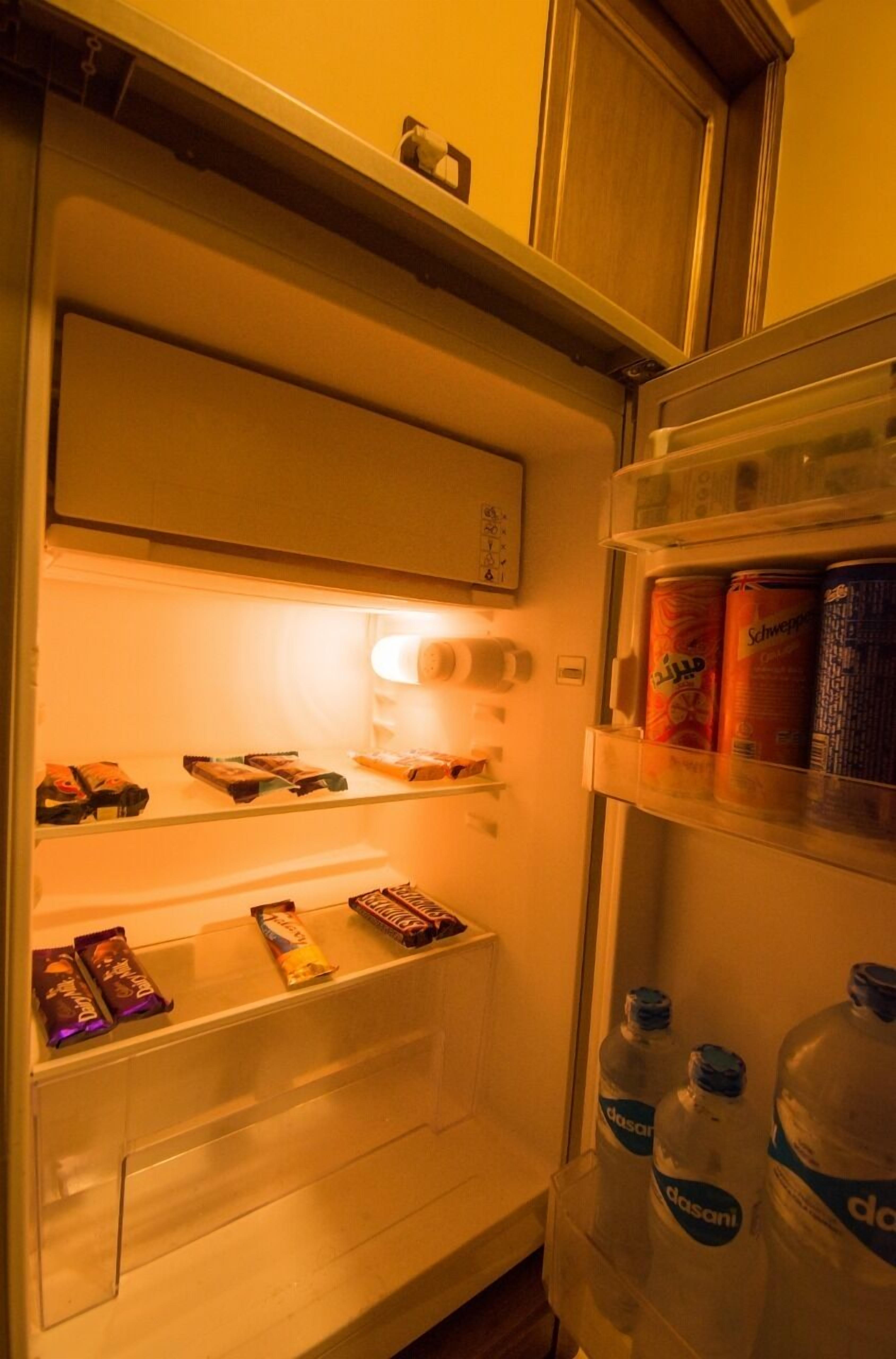 Un refrigerador con estantes que contienen aperitivos, una botella de agua Dasani y una lata de Schweppes.