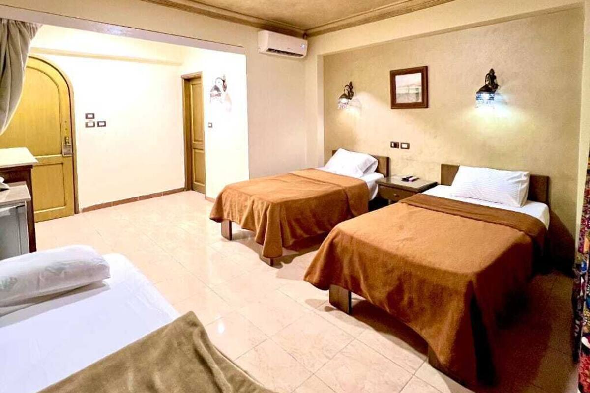 A hotel room with two beds, a desk, a chair, and a door leading to another room.