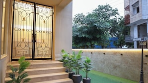 A building entrance with a double door, steps leading up to it, and potted plants on the steps. - Millora Cyber Suites (Gurugram)