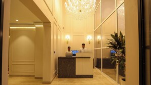 A reception desk with two staff members, a chandelier, and a potted plant. - Millora Cyber Suites (Gurugram)
