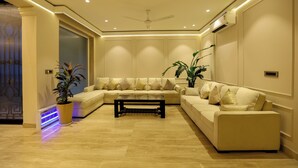 A modern living room with a sectional sofa, a coffee table, and two potted plants. - Millora Cyber Suites (Gurugram)