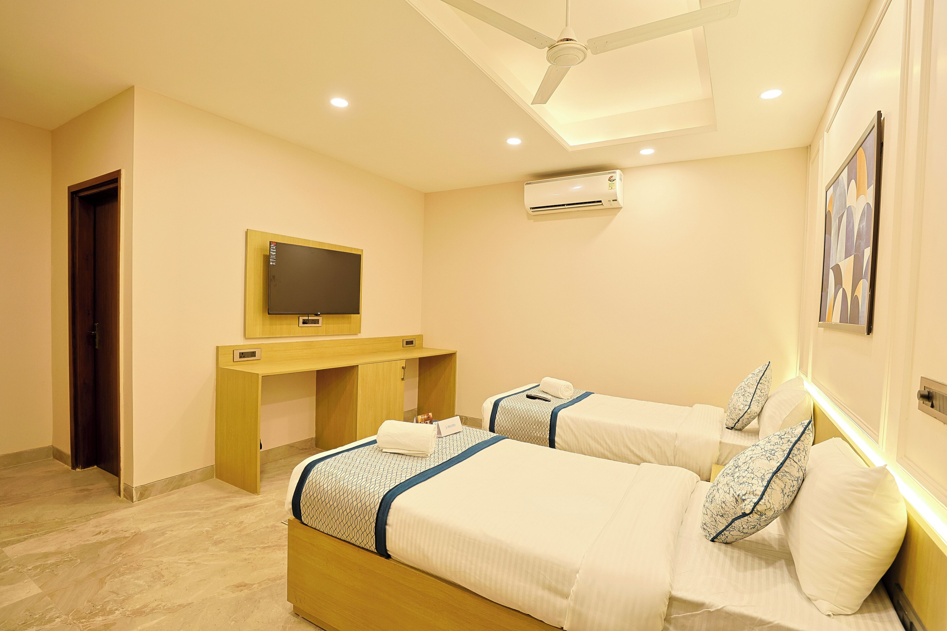A hotel room with two beds, a desk, a television, and an air conditioning unit.