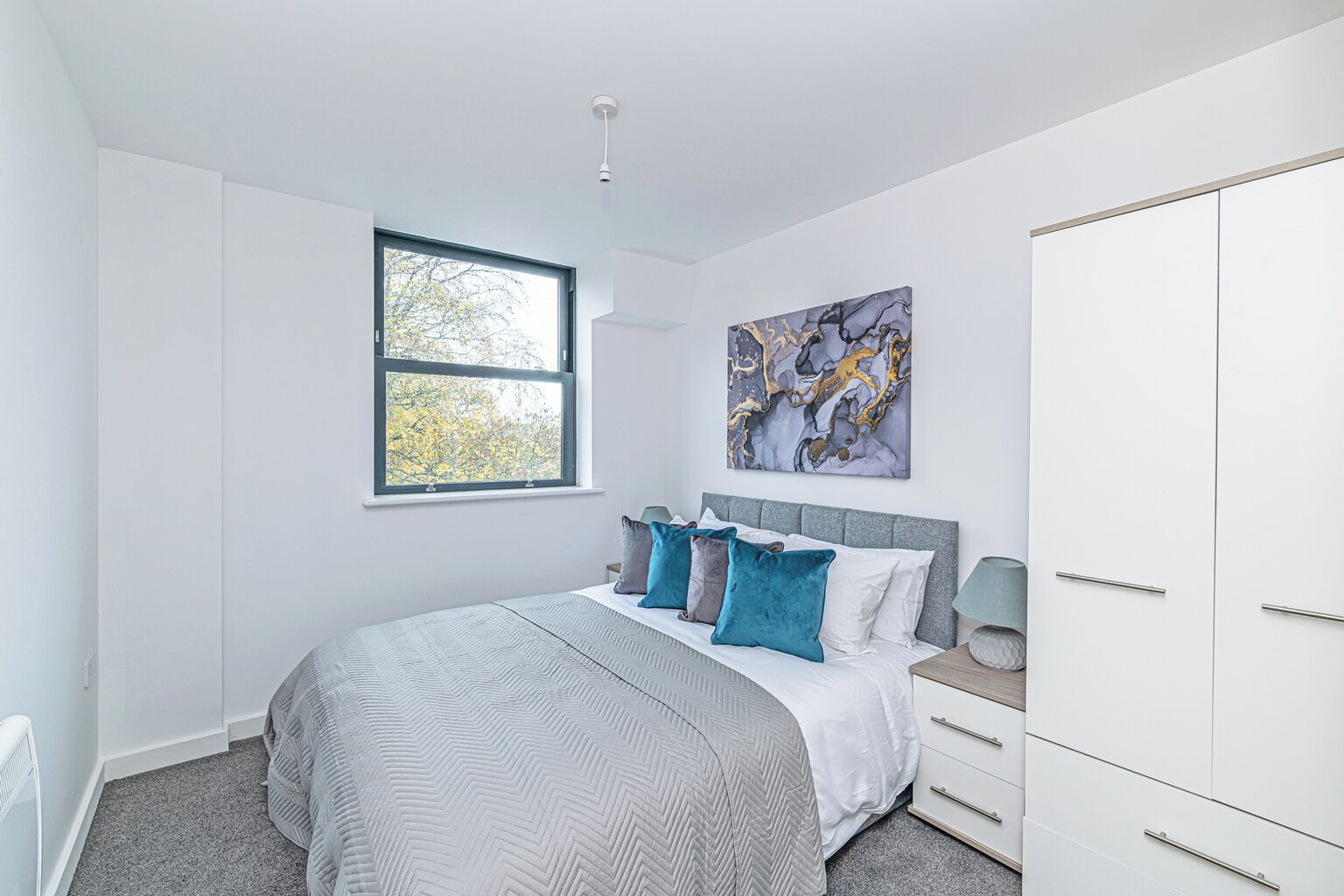 A bedroom with a bed, a window, a painting, and a wardrobe.