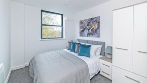 Een slaapkamer met een bed, een raam, een schilderij en een kledingkast.