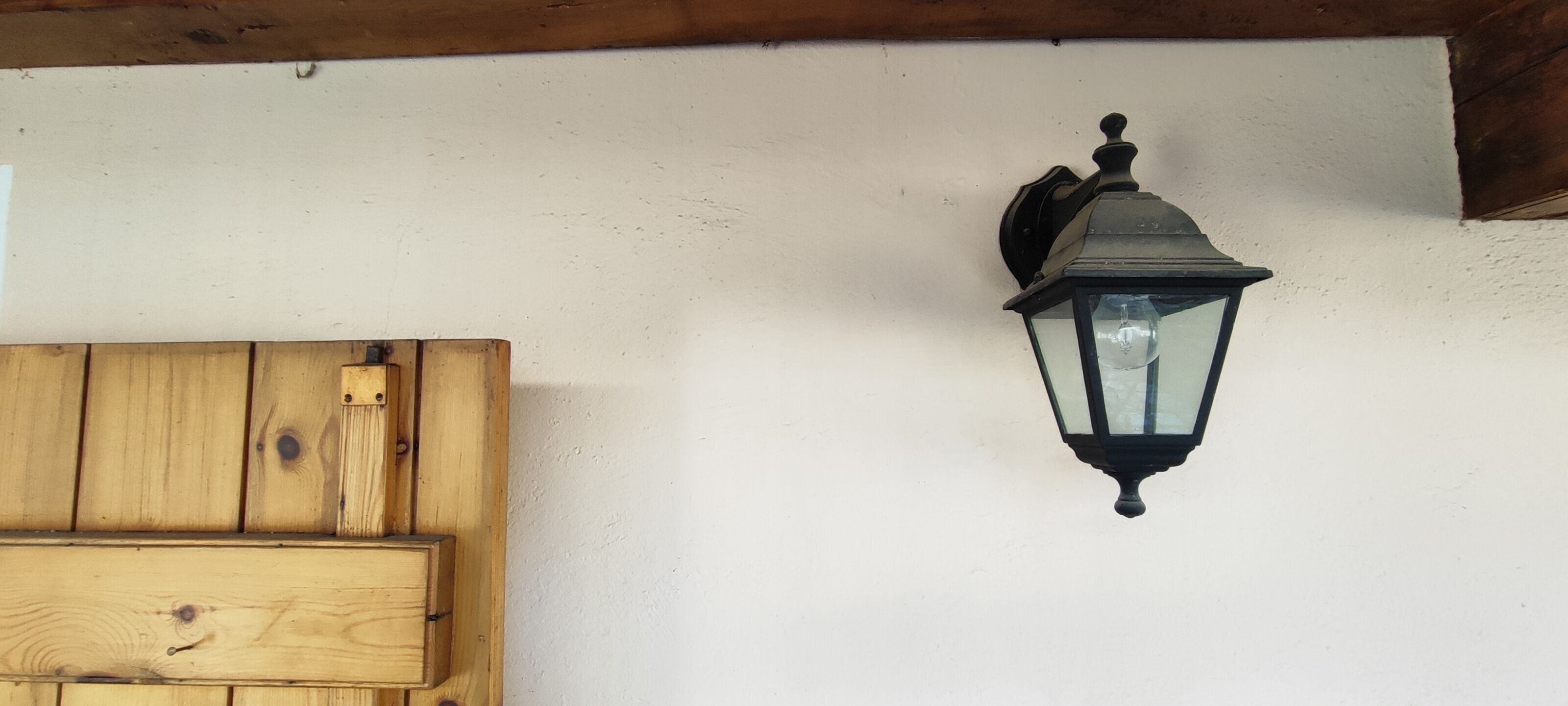 Een houten deur met een metalen grendel en een zwart wandlamp.