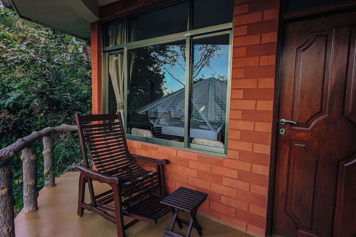 A wooden chair and a small table outside a house with a brick wall and a large window.