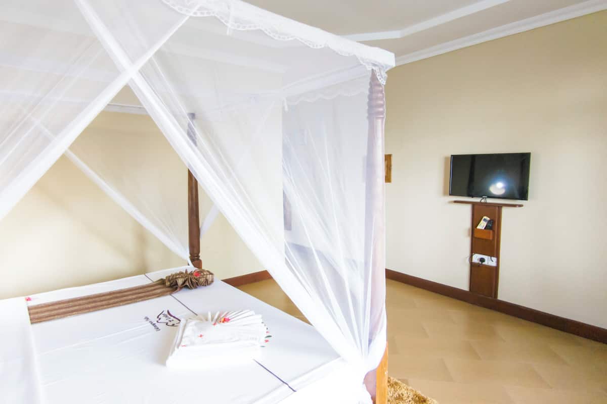 A room with a bed under a white canopy, a television on a wooden stand, and a tiled floor.